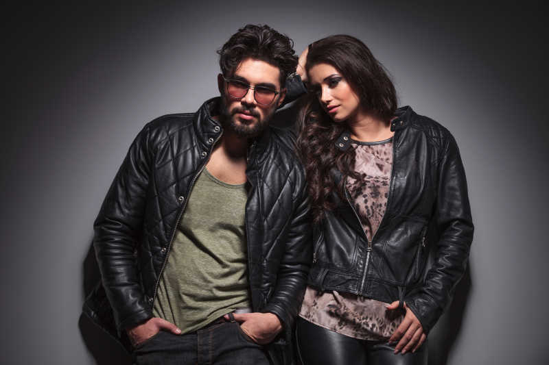 时尚男子双手倚在灰色墙壁上他的女朋友正倚在他身上