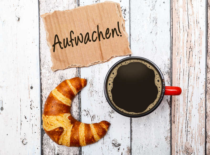 白色桌面上的牛角包咖啡和早安问候语