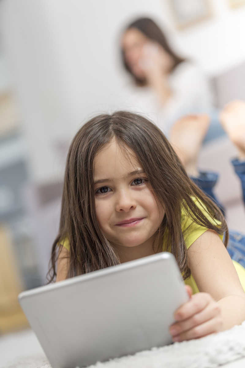 趴在白色地摊上手拿平板电脑的女孩