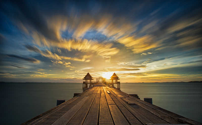 日出-日落背景下的水面上的木制桥梁