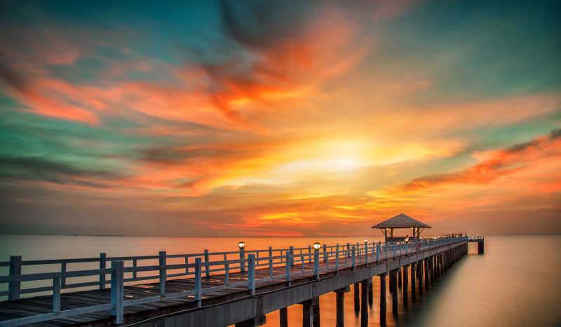 日出-日落背景下的水面上的带围栏的木制桥梁