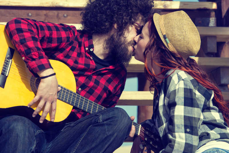 手拿吉他的年轻男子和女友在楼梯台阶上接吻
