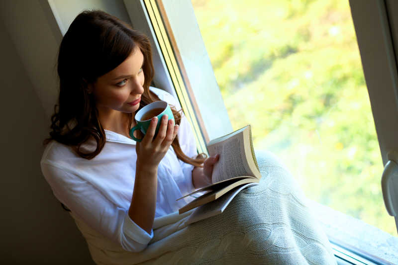 在客厅窗边轻松看书的年轻女子