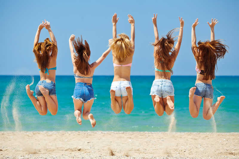 海滩上放松的青少年女孩跳起来