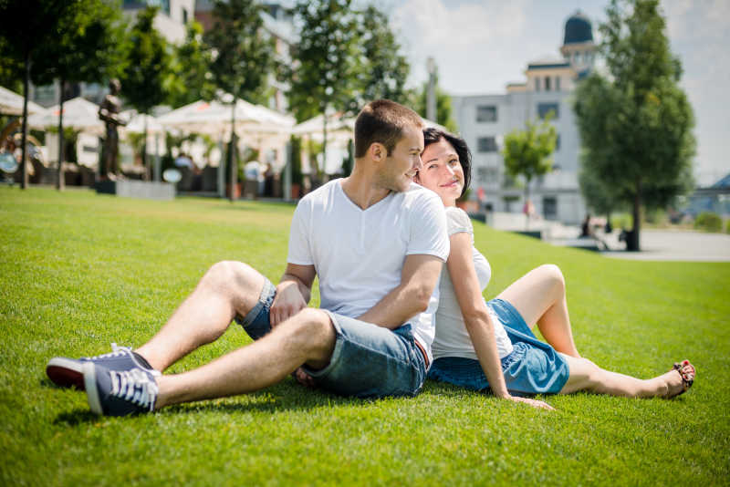 背靠背坐在草地上的情侣