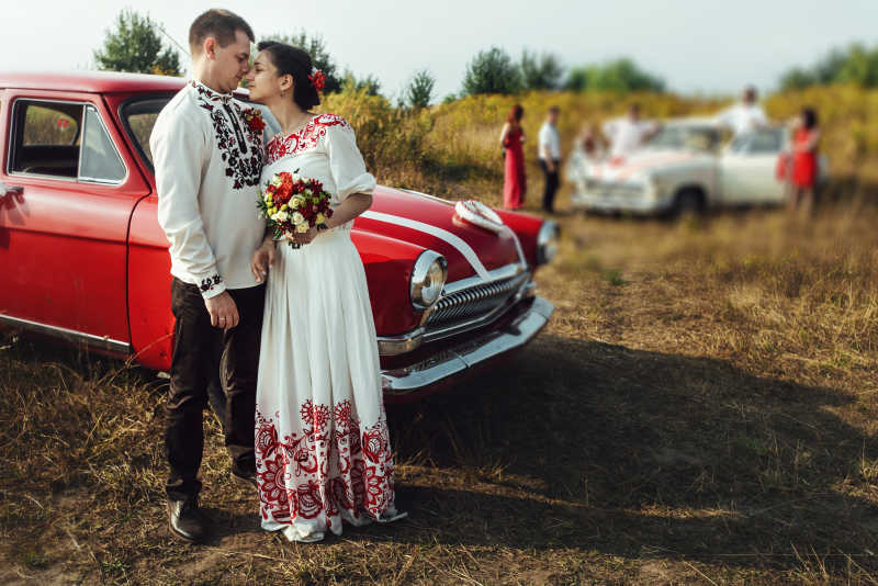 站在红色汽车旁的新郎和新娘
