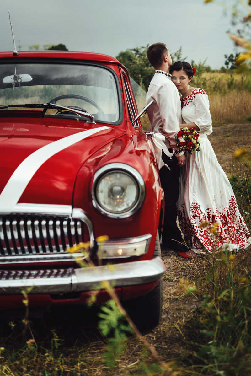 红色复古汽车旁相拥的新娘和新郎