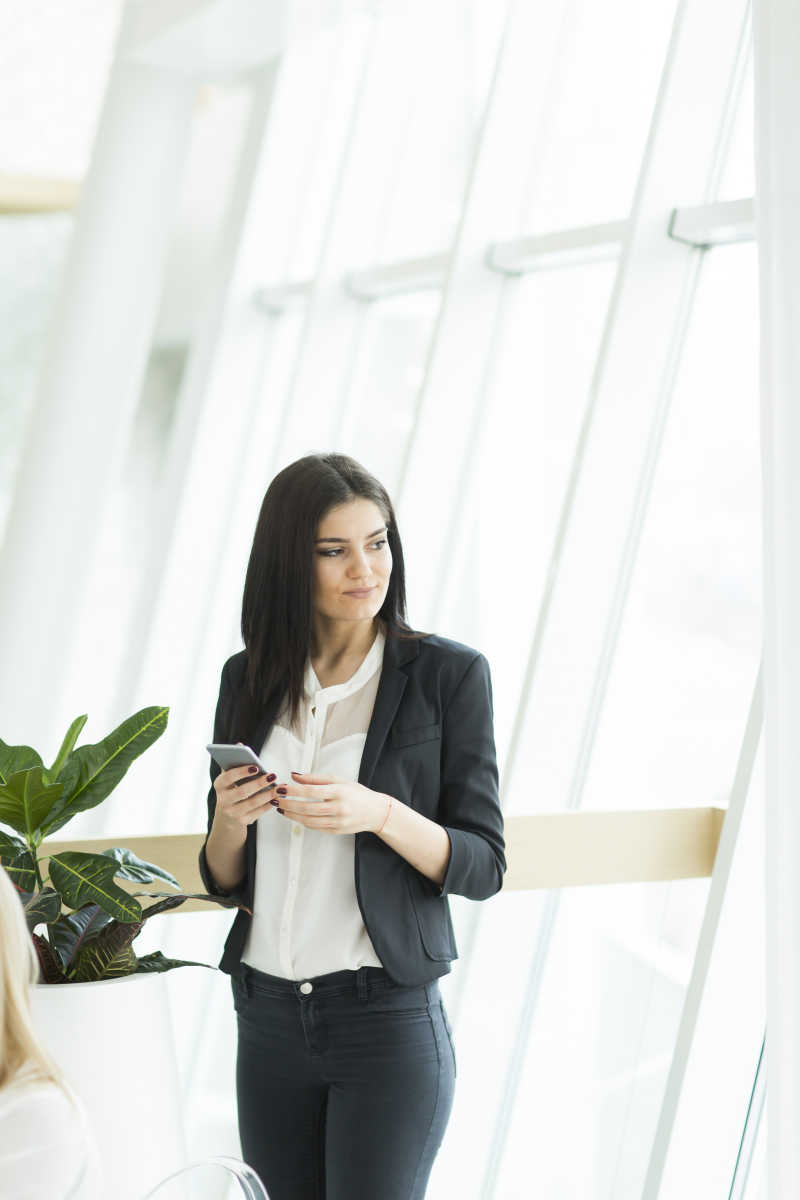 站在窗户边拿着手机的女商人