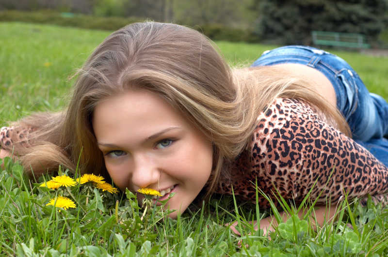 漂亮女孩在绿色草地上闻到蒲公英的味道