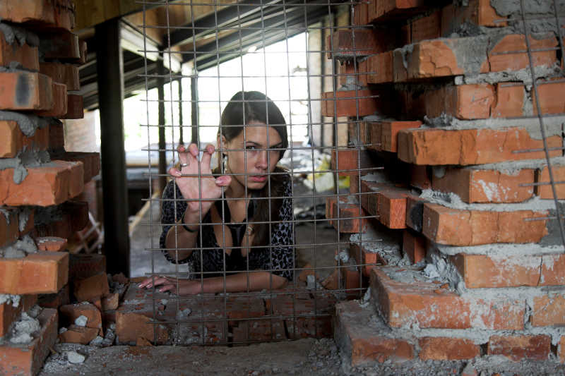 女人用手抓着红砖墙中的护栏网