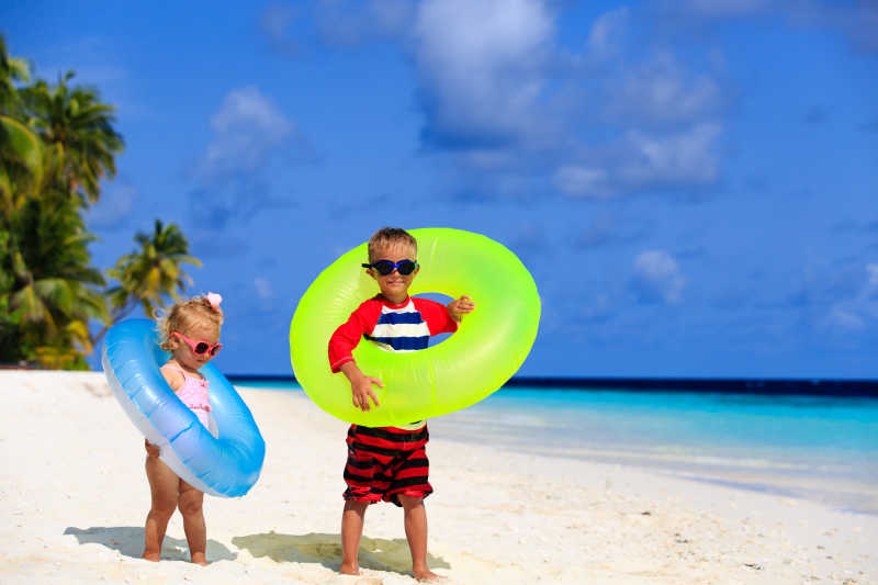 两个带着泳圈的小孩站在热带海滩上