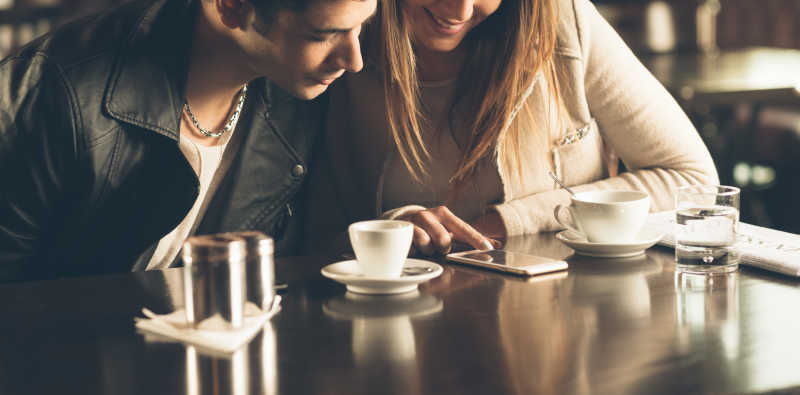 在咖啡馆的年轻男女一边喝咖啡一边使用智能手机