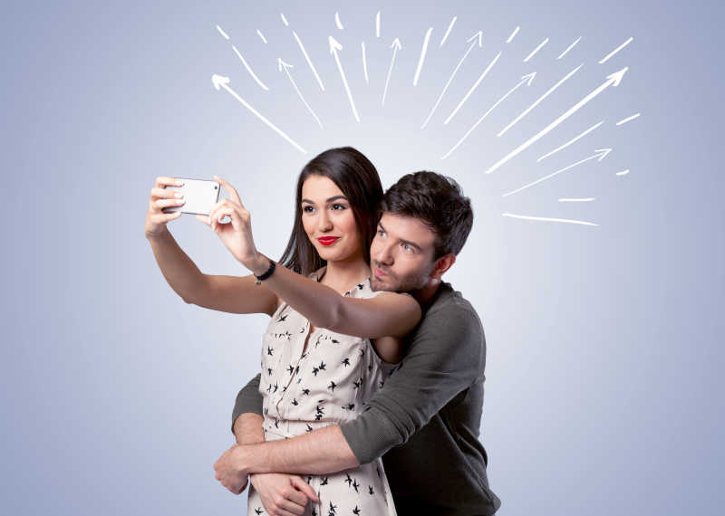 开朗的年轻夫妇在白色线条和箭头指向天空为背景在自拍