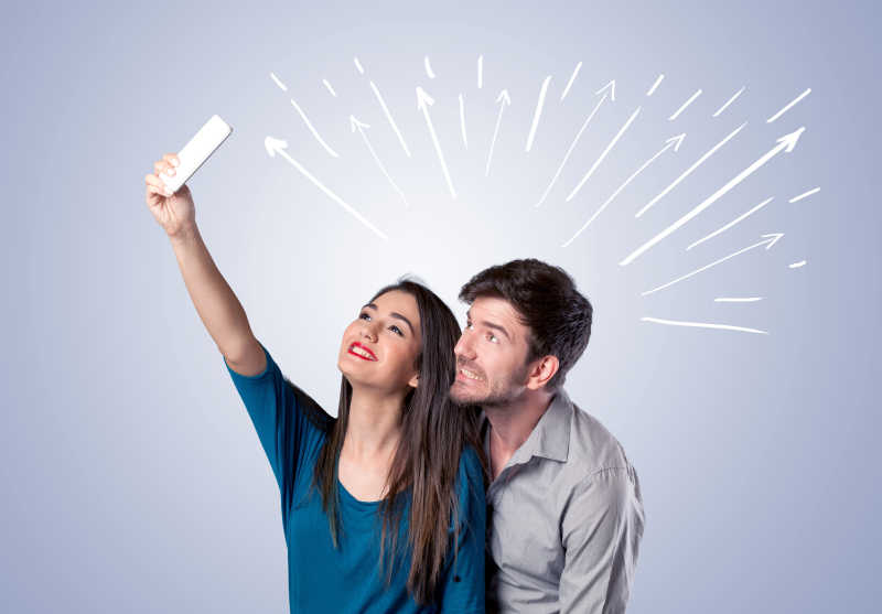 在白色线条和箭头指向天空背景下自拍的开朗的年轻夫妇