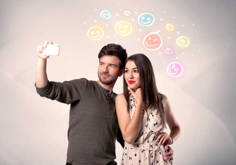 在多姿多彩的幸福笑脸图上面拿着手机自拍的开朗的年轻夫妇