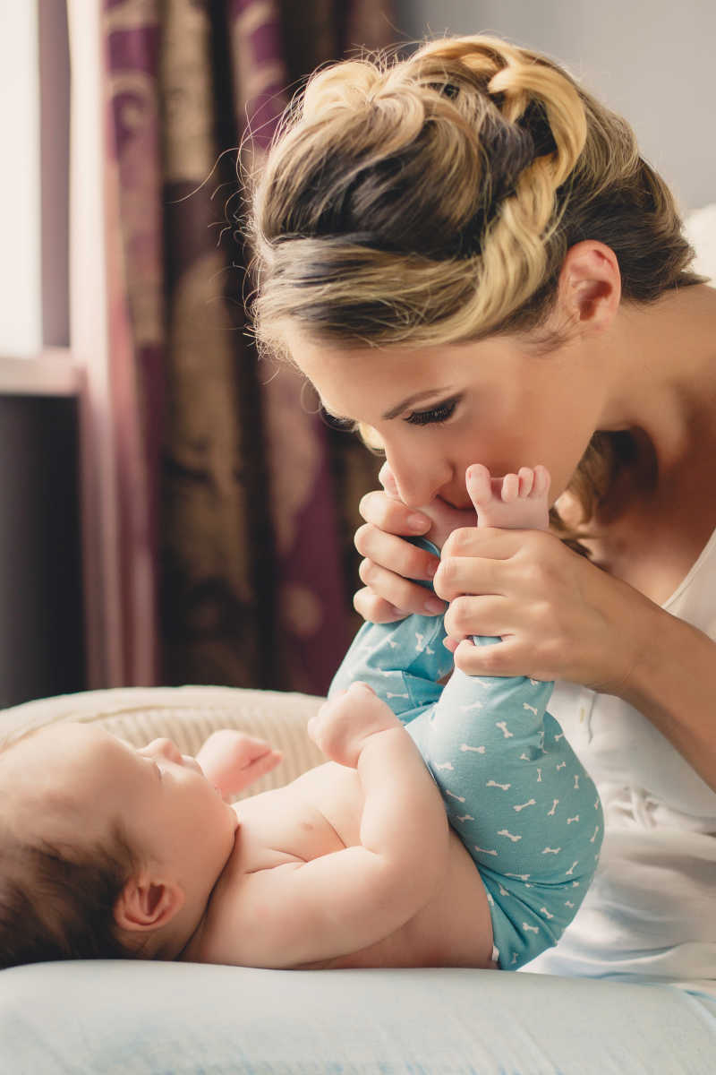 年轻母亲亲吻着新生婴儿的脚丫