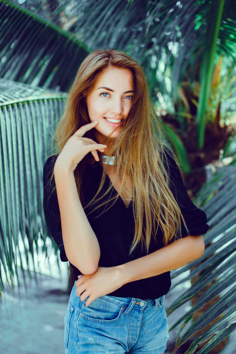 在棕榈树前摆姿势的年轻女孩
