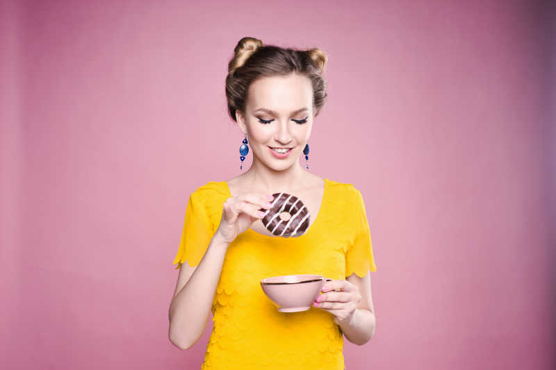 一个年轻女孩拿着甜甜圈在粉红色背景下载