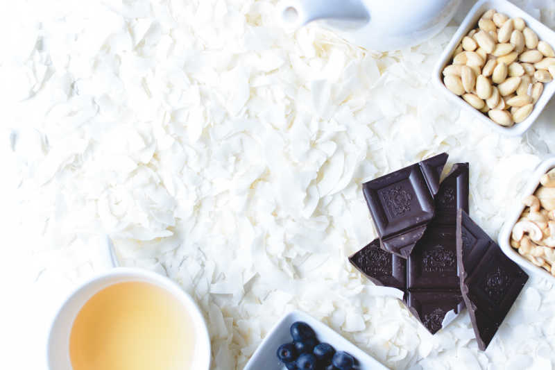 白色背景下散落的白色椰蓉碗装腰果和巧克力