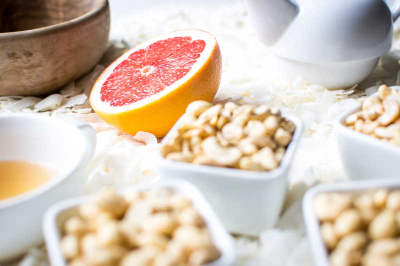 白色桌面上散落的椰蓉上的碗装腰果和橙子