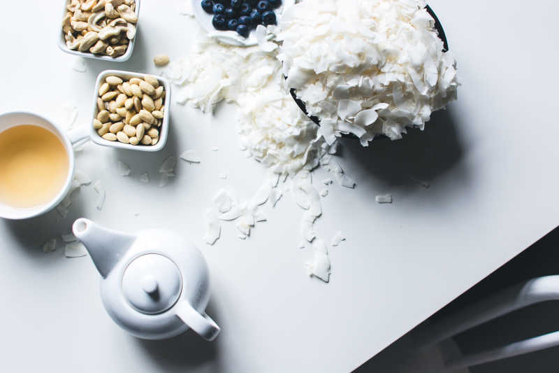 白色桌面上的碗装椰蓉茶水和碗装腰果