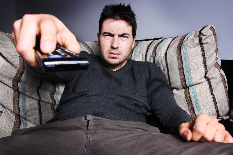 沙发上使用遥控器远程控制的人