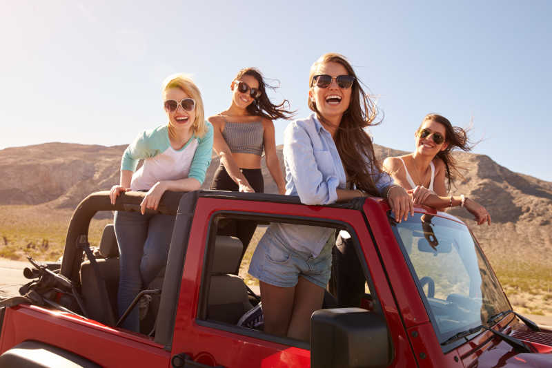 四位女性朋友在公路旅行中站在敞篷车上微笑