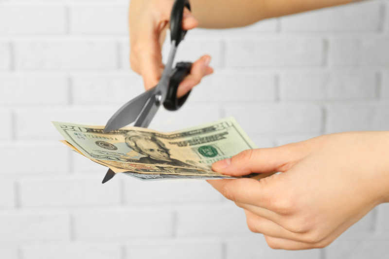 双手用剪刀在白砖背景下切钱