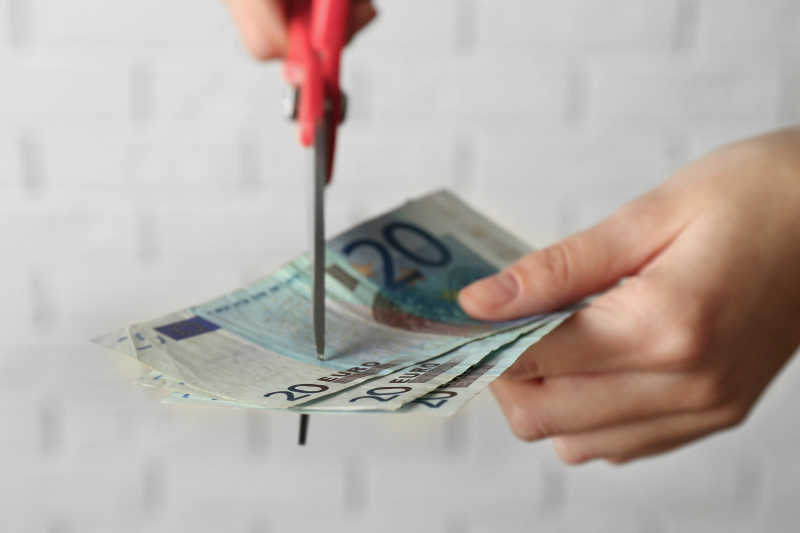 双手用剪刀在白砖墙背景下剪钱