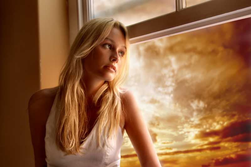 站在窗口前看日落的美女