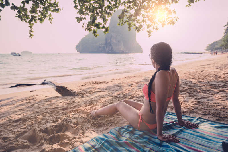 日落十分坐在海岸边上的比基尼美女背影