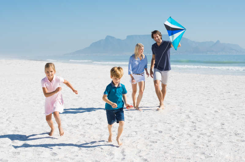 幸福的家庭在海滩上拿着风筝奔跑