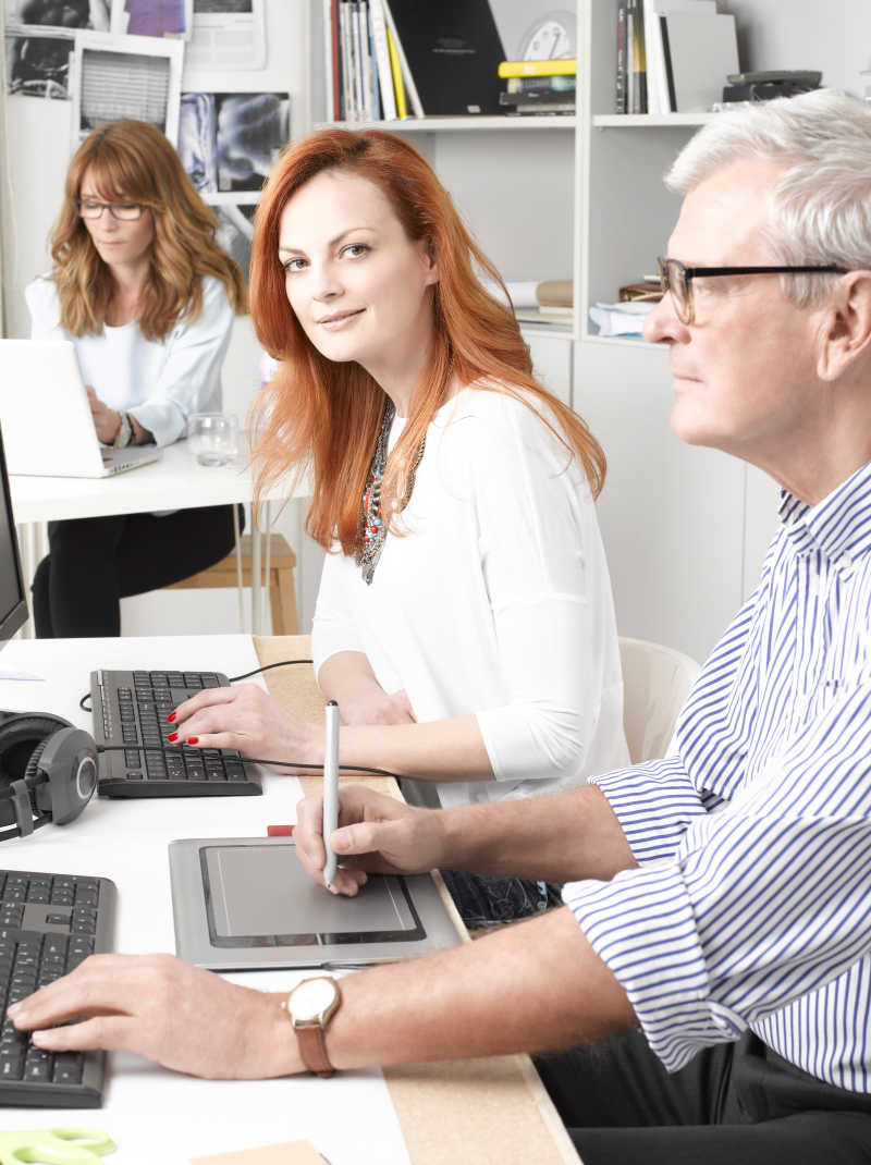 坐在办公桌前与同事一起工作的平面设计师