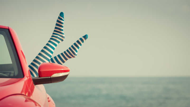 在海滩上放松的年轻女人的双腿伸出红色车窗外