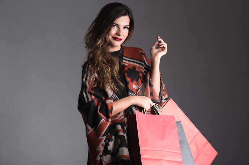 灰色背景下拿着许多购物袋的时尚妇女