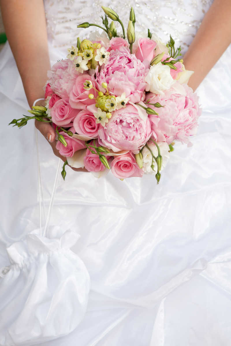 穿着白色婚纱的新娘手中的粉红色和白色花束的婚礼花束