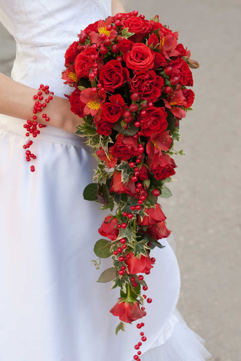 穿这白色婚纱的新娘手中的红玫瑰花束