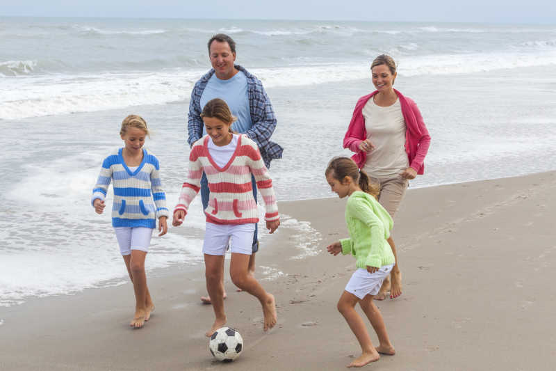 在沙滩上玩足球的家庭