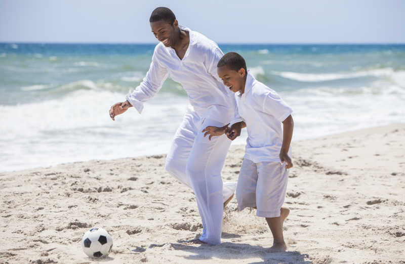 沙滩上踢足球的一对黑人父子