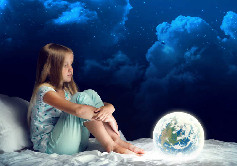 女孩坐在床上看着发光的地球仪