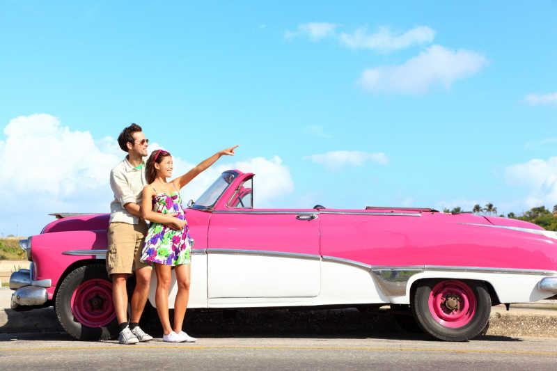 年轻的情侣站在粉色复古车旁