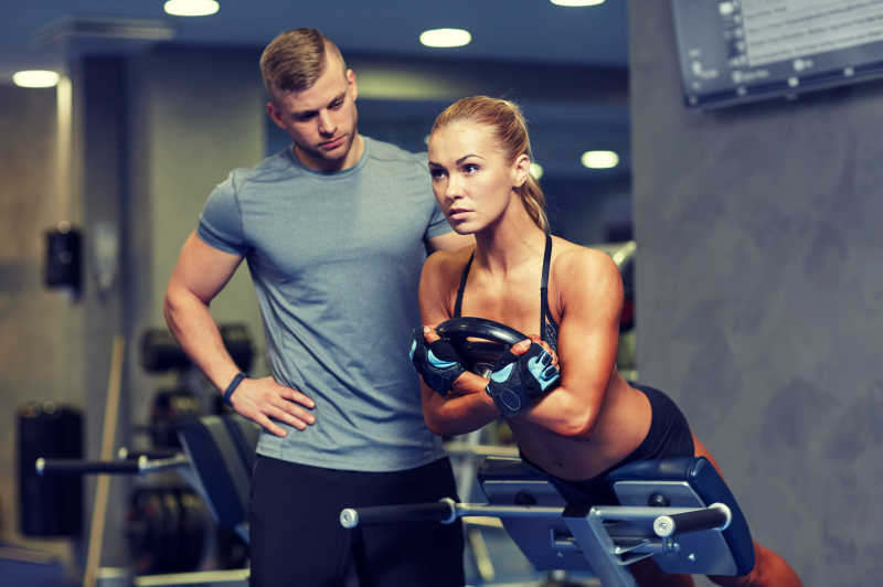 健身房教练指导女孩锻炼背部肌肉