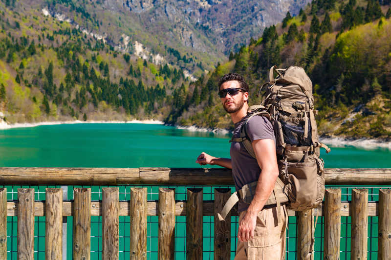 背包徒步旅行者在湖边的木围栏旁
