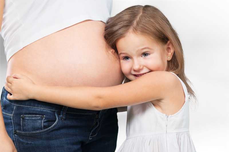 正在抱着孕妇妈妈肚子的小女孩