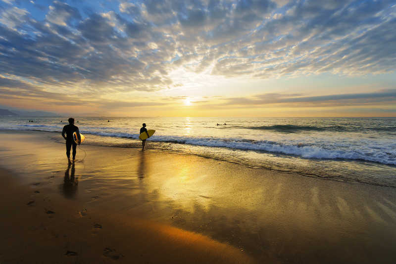 日出-日落背景下走在沙滩上拿着冲浪板的人