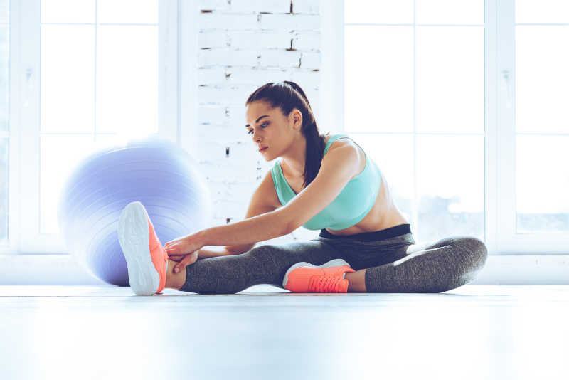 穿着运动服的美女在地板上做伸展运动