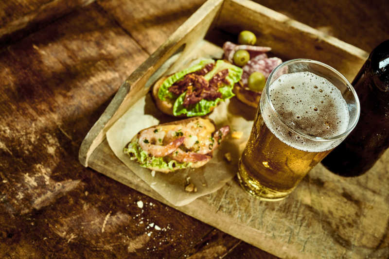 木托盘上的一杯啤酒和用纸包着的小吃