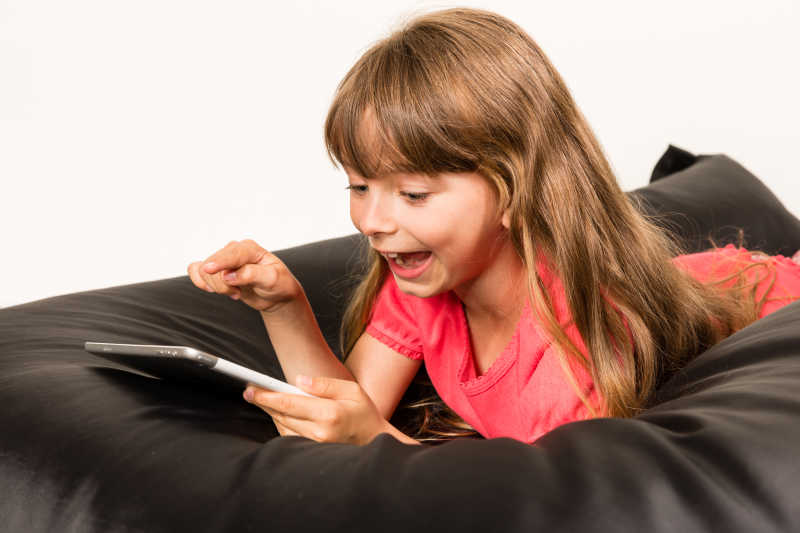 小女孩趴在沙发上开心的玩着电脑