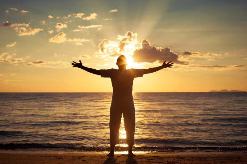 日落时分双手举着站在海岸边的男人