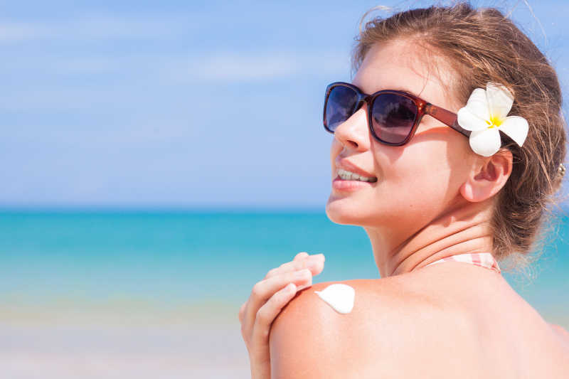 戴太阳镜的女人在涂肩上的防晒霜